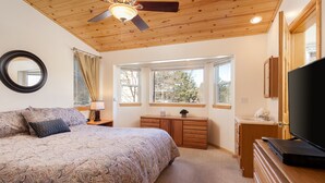 A bedroom with a bed, a dresser, a television, a ceiling fan, and a window.