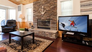 A living room with a stone fireplace, a television, a black leather chair, and a patterned rug.