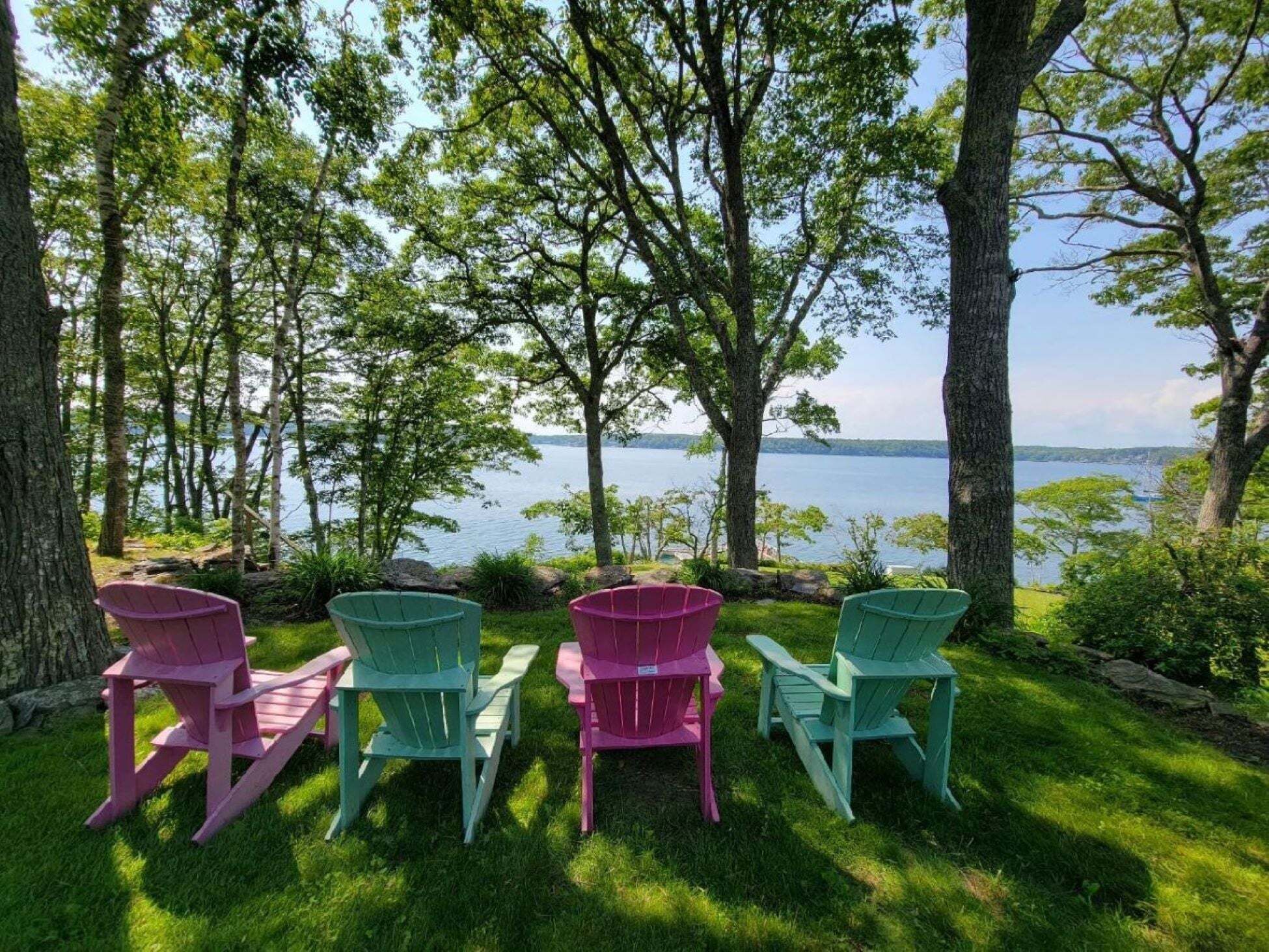 A lakeside view with four Adirondack chairs in green and pink colors.