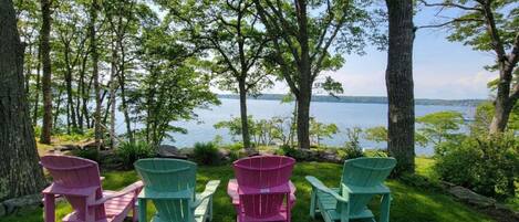A lakeside view with four Adirondack chairs in green and pink colors.