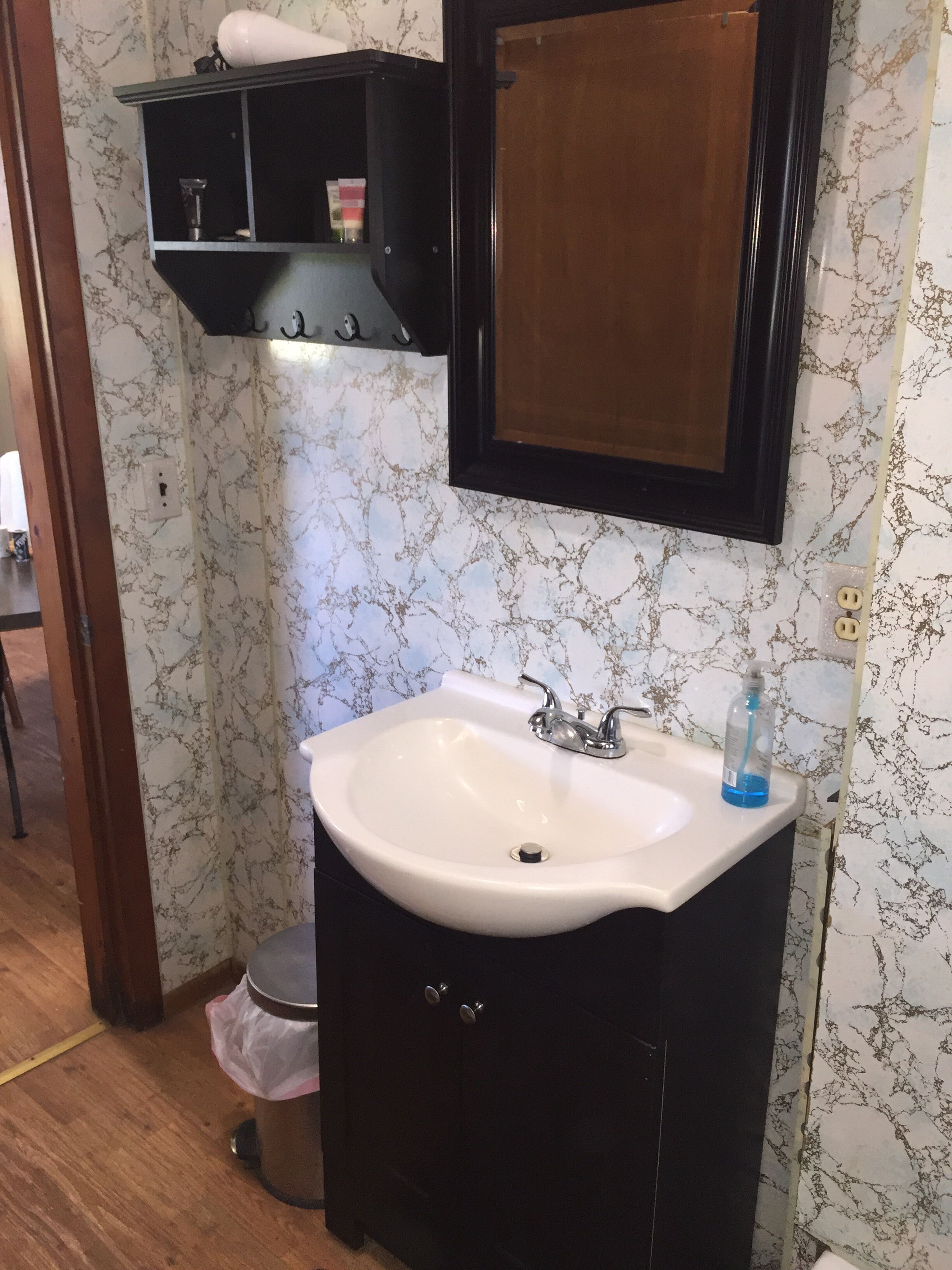 A bathroom with a white sink, black cabinet, and marble-patterned walls.