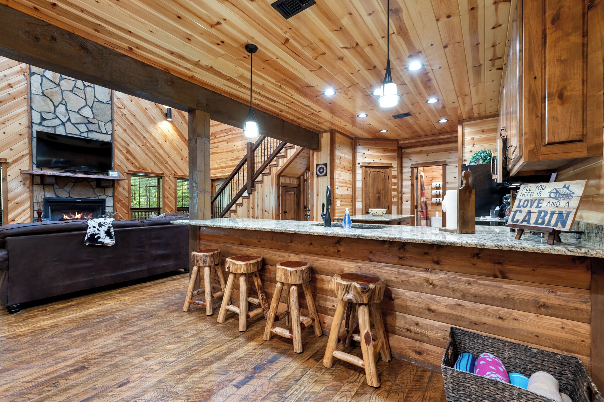 A cabin interior with a stone fireplace, wooden ceiling, and a bar area with stools.