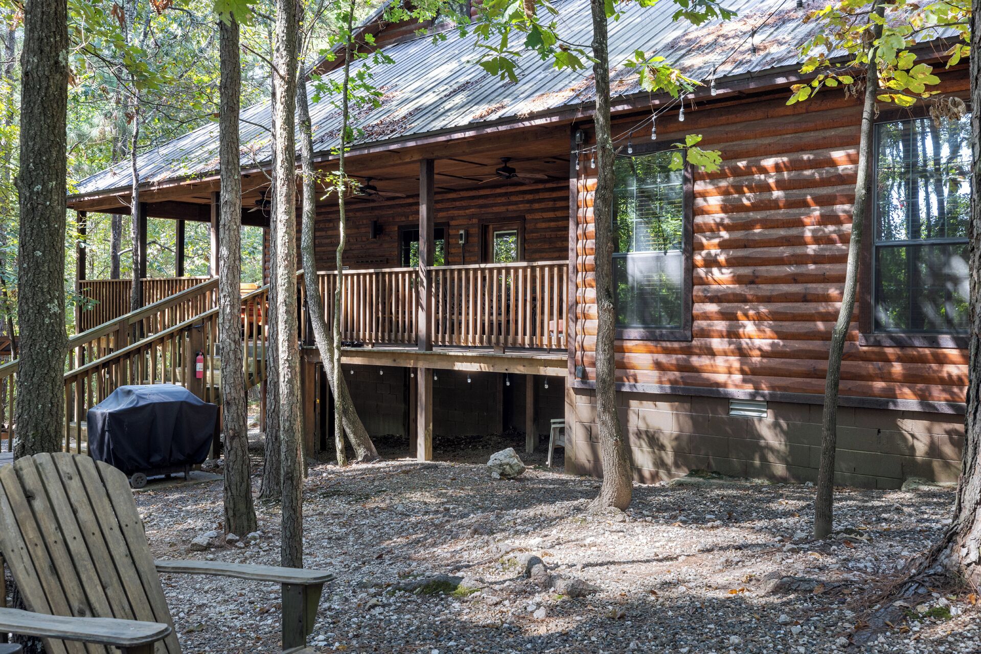A rustic cabin with a wooden deck, a covered grill area, and a bench.