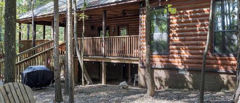 A rustic cabin with a wooden deck, a covered grill area, and a bench.