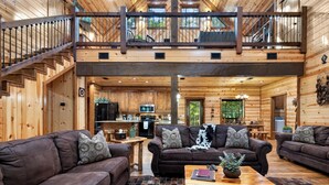 A spacious log cabin interior with a living area, kitchen, and upper deck.