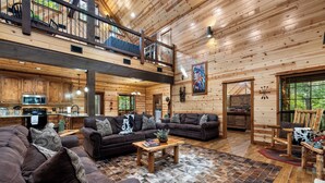 A spacious log cabin interior with a living area, a kitchen, and a balcony.