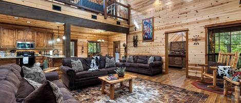 A spacious log cabin interior with a living area, a kitchen, and a balcony.