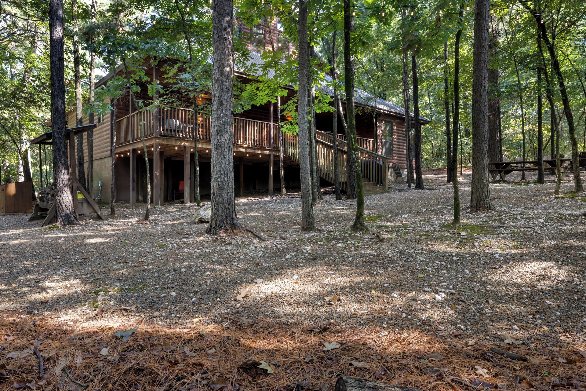 A rustic cabin with a wooden deck and multiple levels, surrounded by trees in a forested area.
