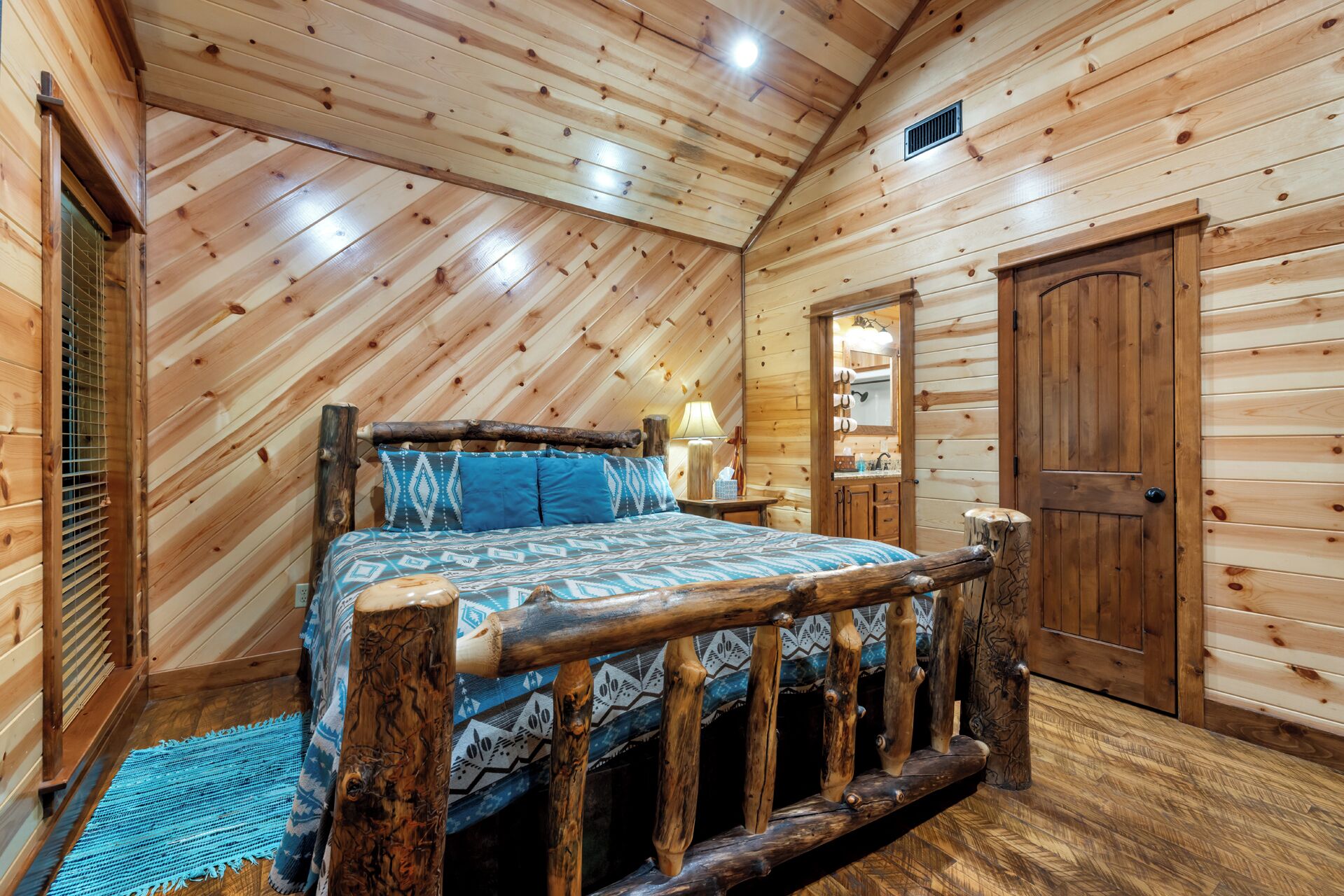 Ein Schlafzimmer einer Holzhütte mit einem Bett, einem Nachttisch, einer Lampe und einer Tür.