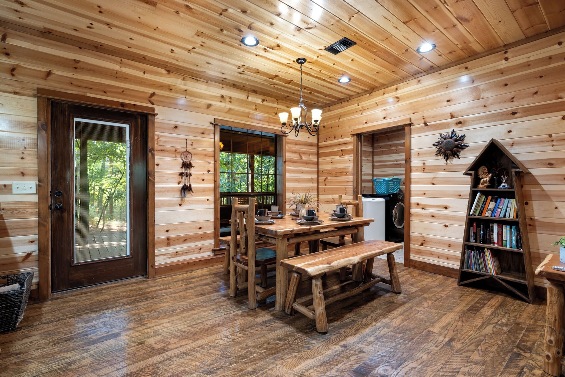 Un intérieur en bois comprenant une table à manger, des chaises, un banc, une bibliothèque et un luminaire suspendu au plafond.
