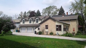 Ein zweistöckiges Wohnhaus mit Garage, einem Vorgarten mit Gras und Löwenzahn sowie einem Ziegelkamin.