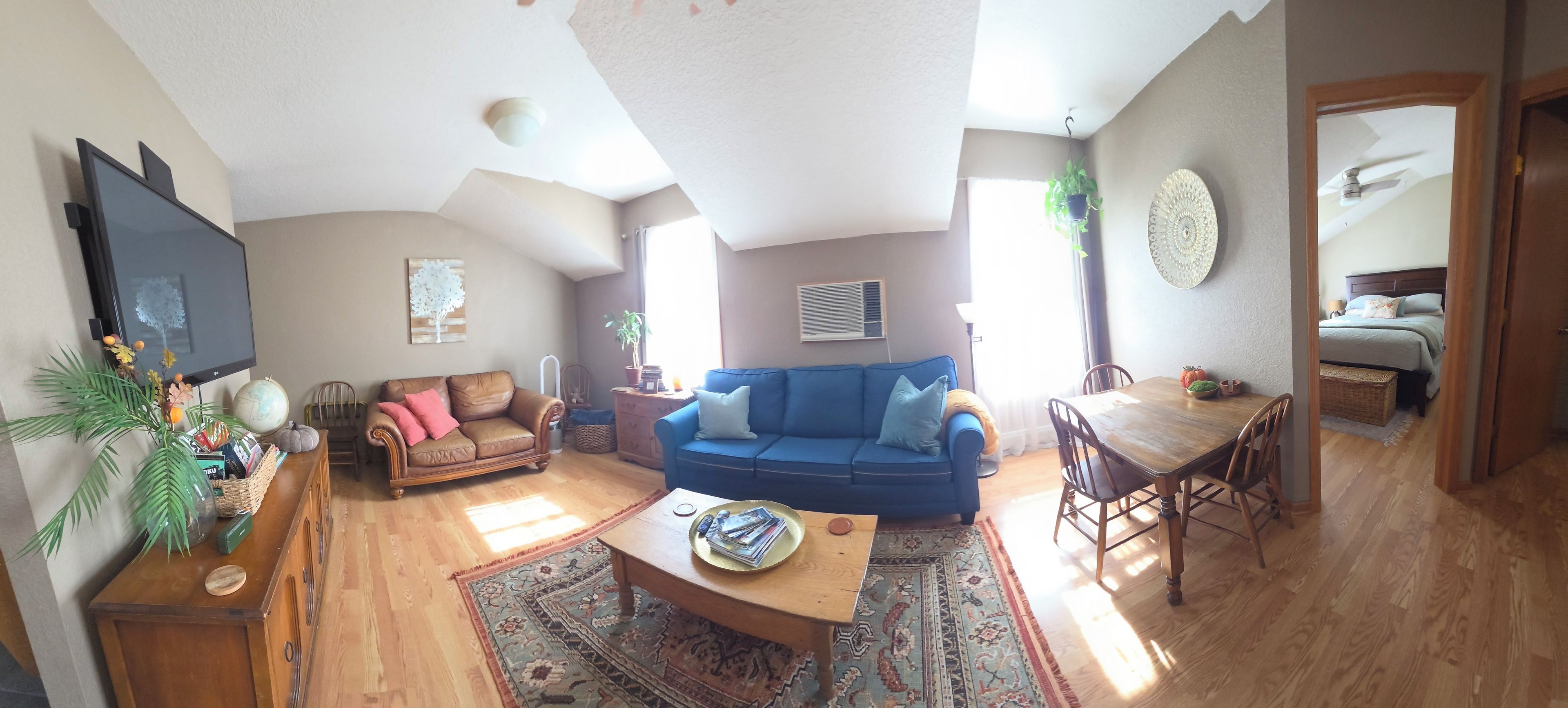 Una sala de estar con un sofá azul, una mesa de centro de madera y un televisor. Hay un comedor con una mesa y sillas.
