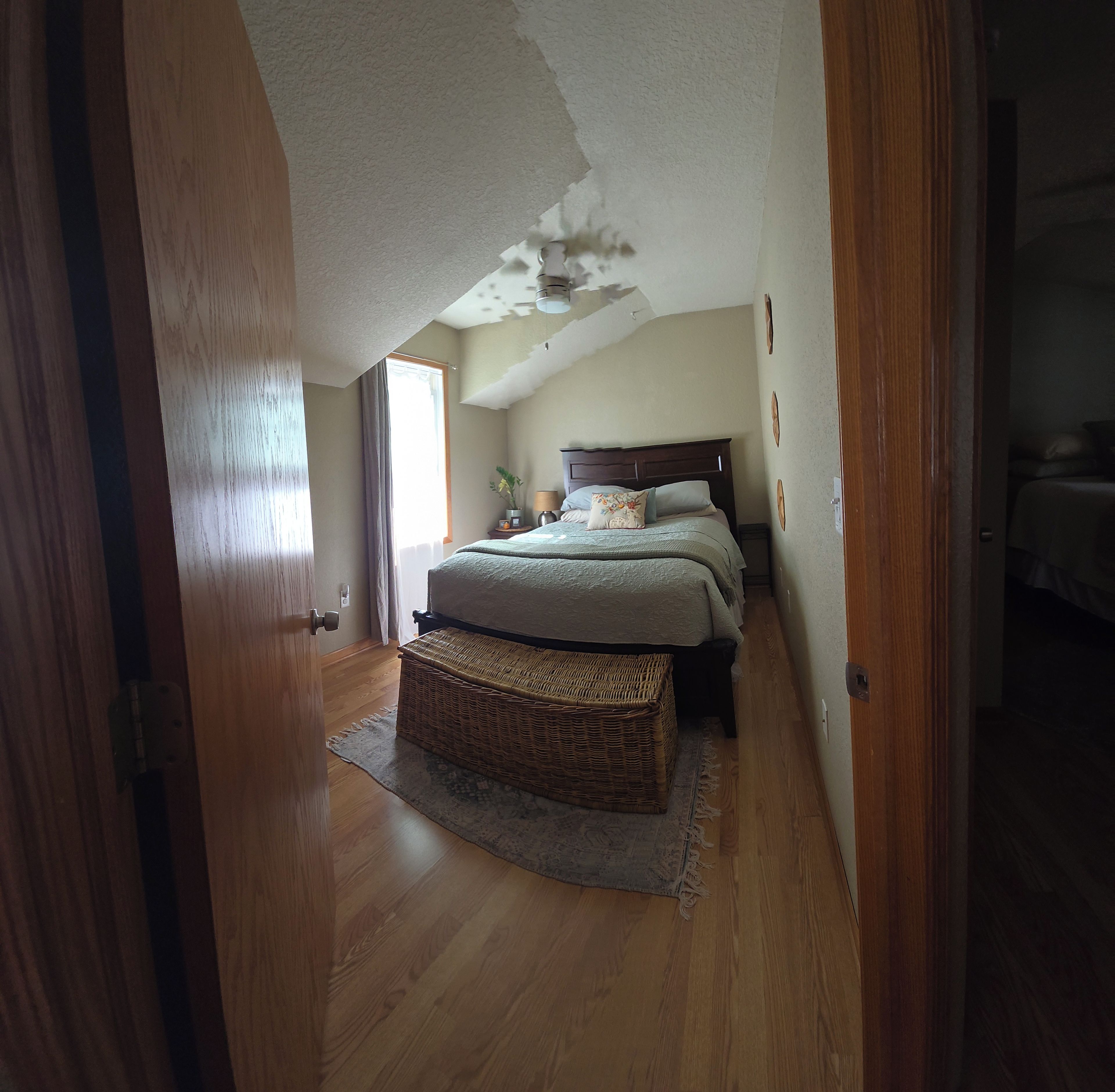 A bedroom with a sloped ceiling, a bed with a headboard, a bedside table, a lamp, and a wicker basket.
