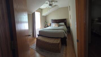 A bedroom with a sloped ceiling, a bed with a headboard, a bedside table, a lamp, and a wicker basket.