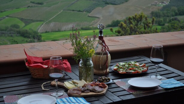A table set with food and drinks, a vase with flowers, and a view of a green landscape.