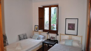 A bedroom with two beds, a small table, and a window with wooden shutters.
