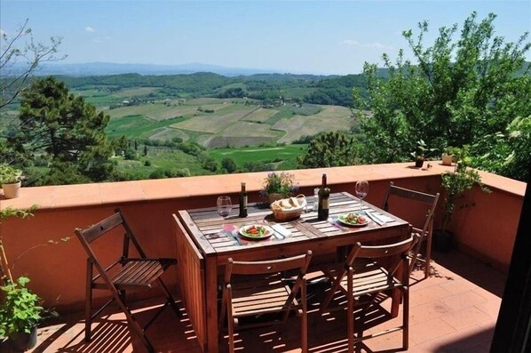 A wooden table set with plates, wine glasses, and a bottle on a terrace overlooking a green landscape. - INDEPENDENT HOUSE LARGE TERRACES & SPECTACULAR VIEWS in CENTER W. PARKING (Montepulciano)