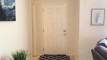 A hallway with a white door, a doormat, a potted plant, and a framed picture on the wall.