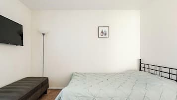 A bedroom with a bed, a bench, a floor lamp, and a framed picture on the wall.