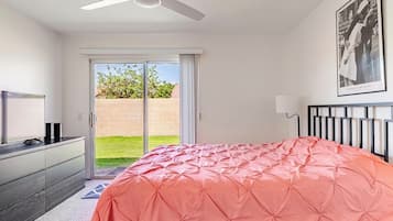 A bedroom with a bed, a ceiling fan, a television, and a sliding glass door leading to a balcony.