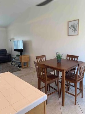 A dining area with a wooden table and chairs, a small potted plant, and a framed artwork on the wall.