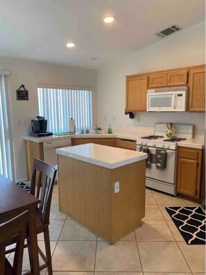 A compact kitchen with wooden cabinets, a microwave, a stove, and a small island.