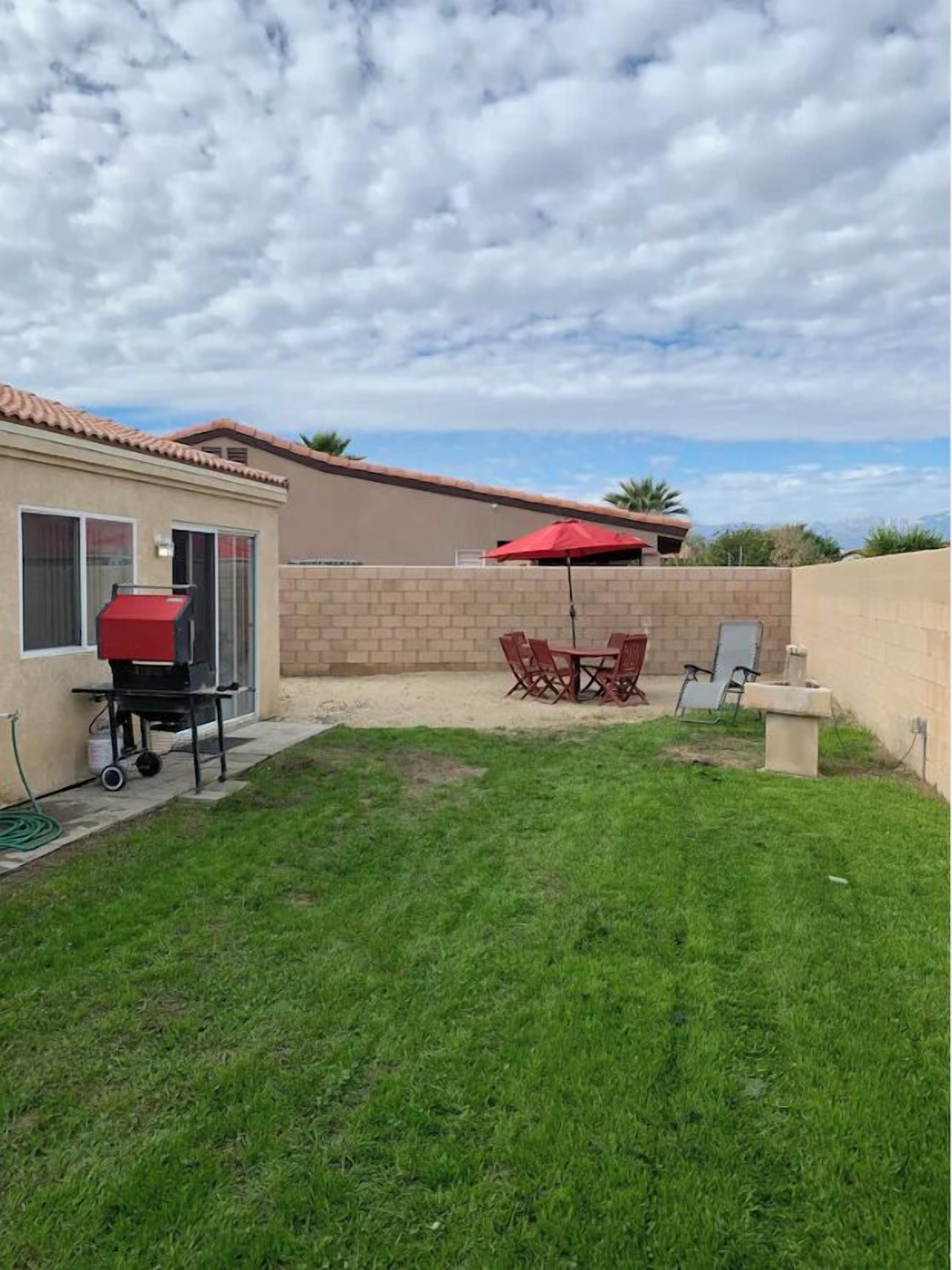 A backyard with a barbecue grill, a dining table with chairs, and a red umbrella.
