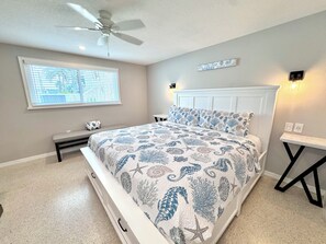 A bedroom with a bed, a ceiling fan, a window with blinds, a bedside table, and a wall-mounted light.