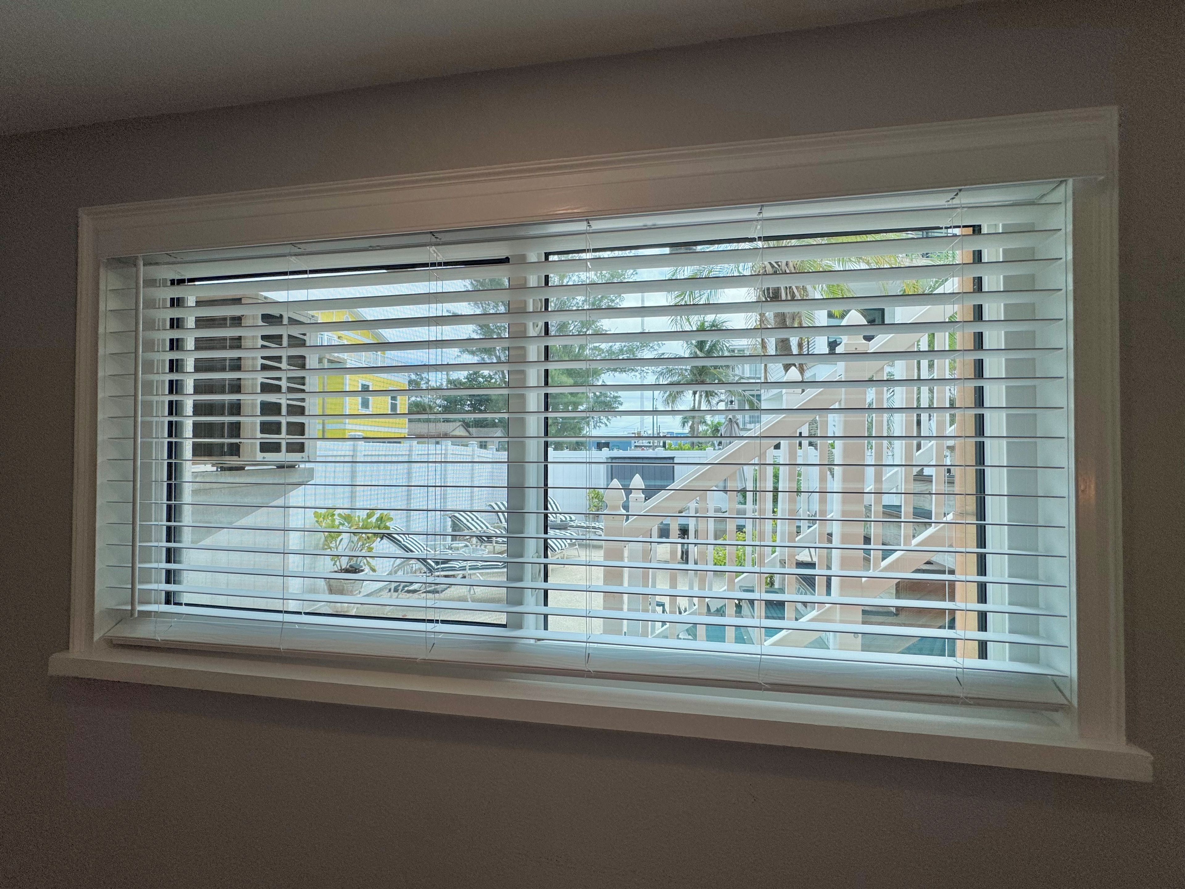 A window with horizontal blinds, a view of outdoor stairs, and a building in the background.