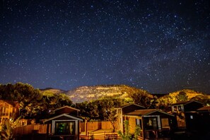 Ein Sternenhimmel über einem Wohngebiet mit Häusern und einer hügeligen Landschaft im Hintergrund.