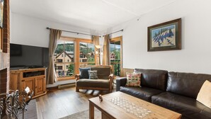 A living room with a wooden coffee table, a leather sofa, a TV, and a window with curtains. - Breckenridge Ski In Ski Out Condo, Great Views, Pool & Hot Tubs, Walk to Town (Breckenridge)