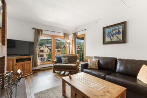 Uma sala de estar com uma mesa de centro de madeira, um sofá de couro, uma televisão e uma janela com cortinas.