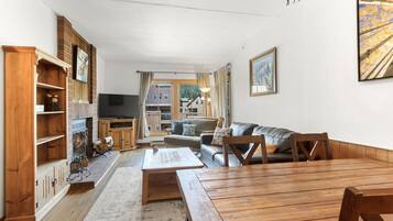 A spacious living room with a wooden dining table, a sofa, and a TV in the background.