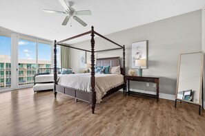 A four-poster bed with a ceiling fan, a bedside table with a lamp, and a large window with a view of buildings. - 2 bedroom penthouse unit, CPH08! Ask about possible DISCOUNTS!! (Orange Beach)