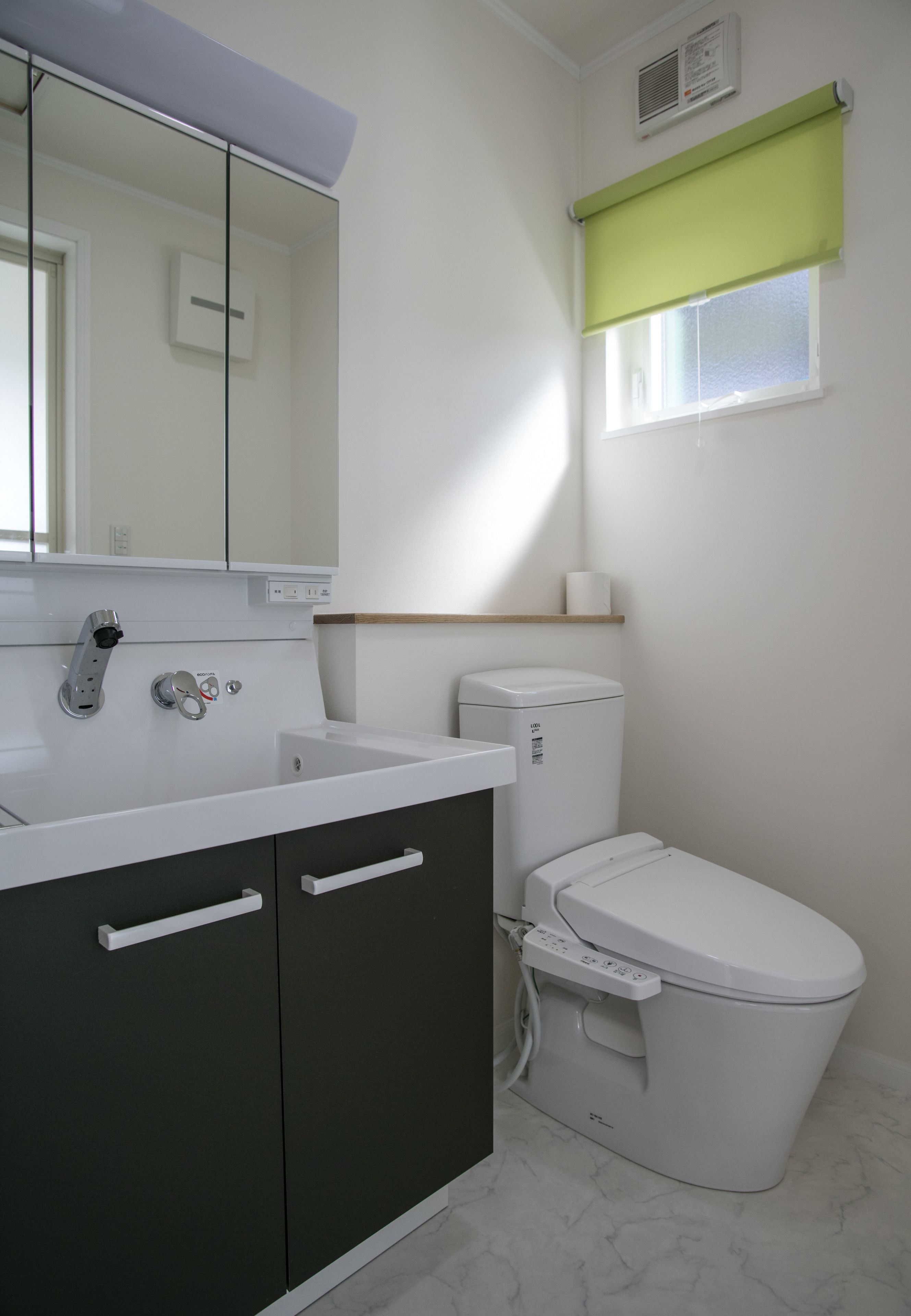 A modern bathroom with a white sink, dark cabinets, a toilet, and a mirror.