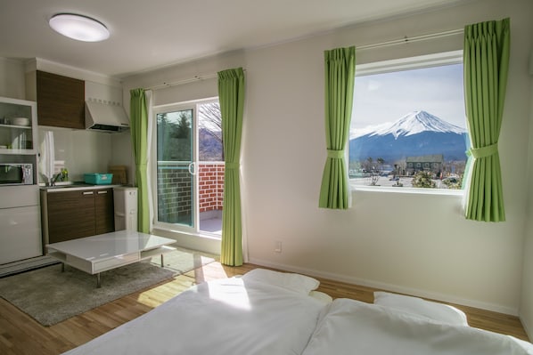 A modern room with a bed, a small table, a kitchenette, and a large window with a view of a mountain. - Cottage Yushin (Fujikawaguchiko)