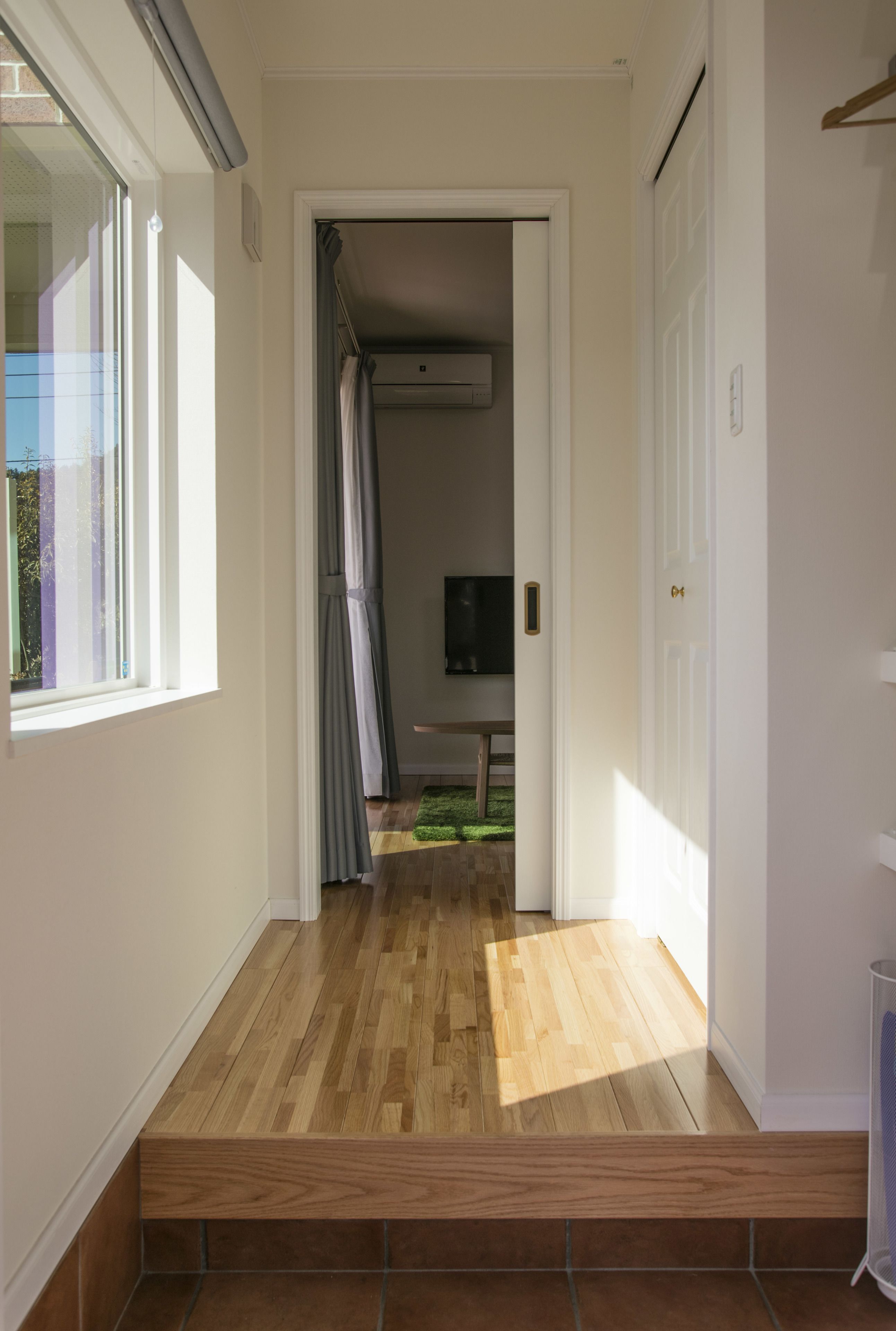 A hallway with wooden flooring, a door on the right, and a window on the left.