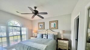 A bedroom with a bed, two bedside tables, a ceiling fan, a window with blinds, and two framed pictures on the wall. - Myrtlewood Condo 1 Mile To Beach - Feel At Home. (Myrtle Beach)