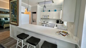 A modern kitchen with white cabinets, a central island with stools, a microwave, stove, and a dishwasher. - Myrtlewood Condo 1 Mile To Beach - Feel At Home. (Myrtle Beach)