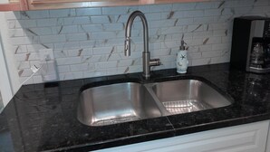 A kitchen with a double sink, a marble backsplash, and wooden cabinets.