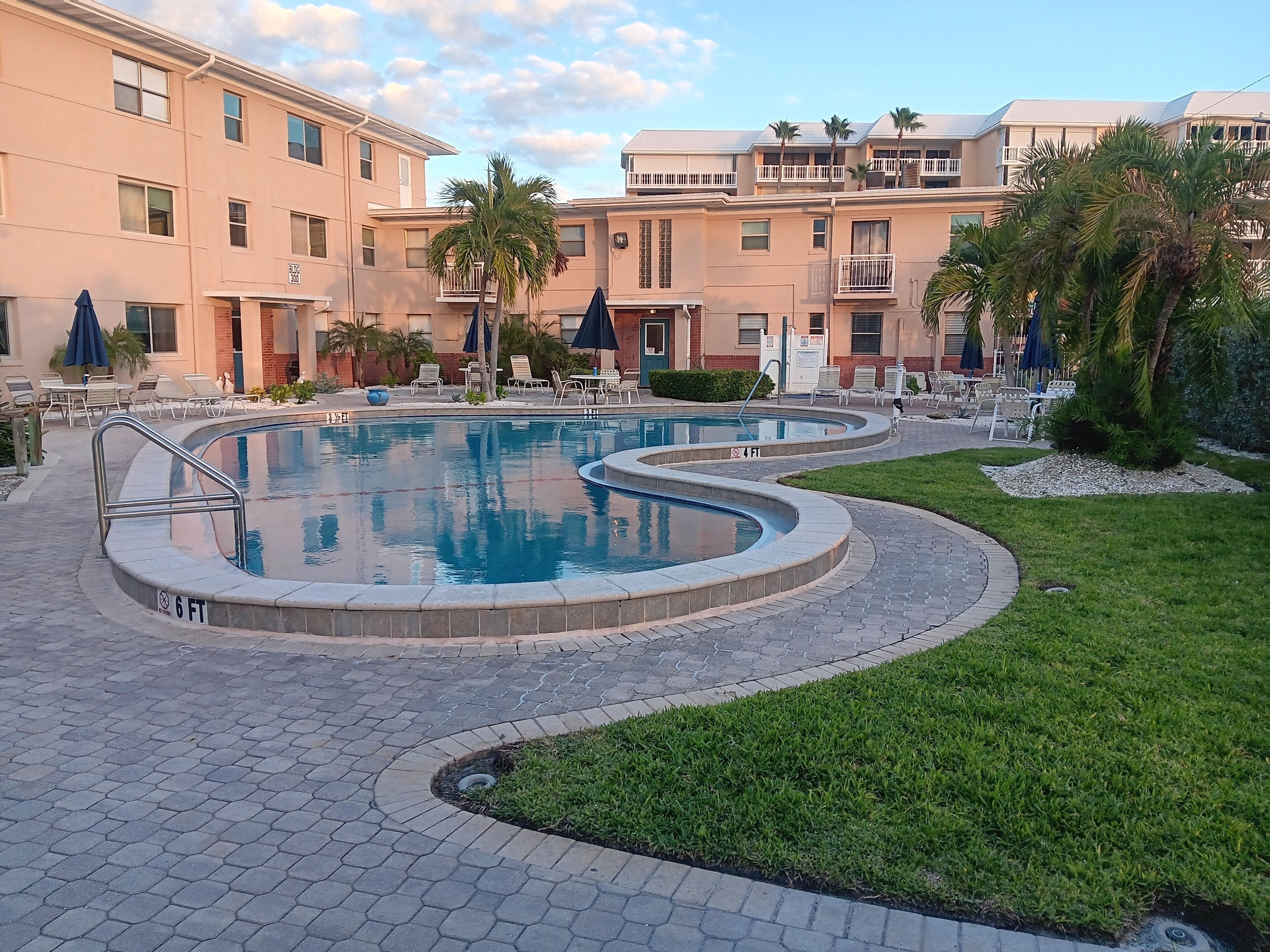 Una piscina con una marca de profundidad de 1.8 metros, rodeada de sillas de descanso y sombrillas, con un edificio al fondo.