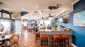 Un restaurante con zona de bar, suelo de baldosas y una pizarra con la carta.