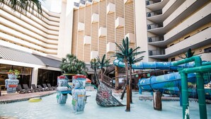 Un vestíbulo de hotel con zona de piscina, incluyendo un tobogán acuático y estatuas decorativas.