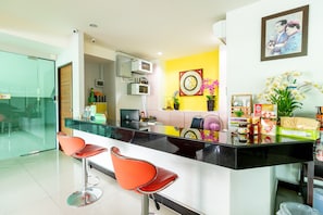 A modern kitchen with a black countertop, two red bar stools, and a yellow accent wall.