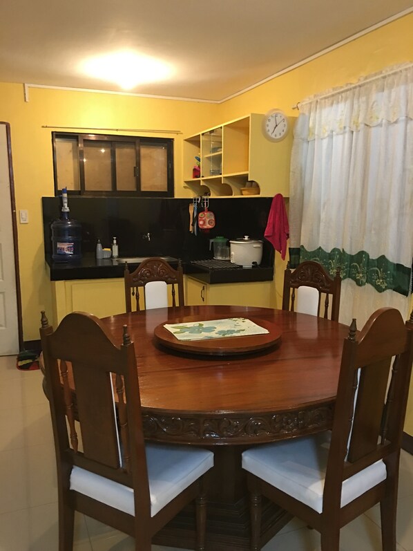 A dining area with a wooden table and chairs, a kitchen in the background, and a clock on the wall. - Pines Mansion (Butuan)