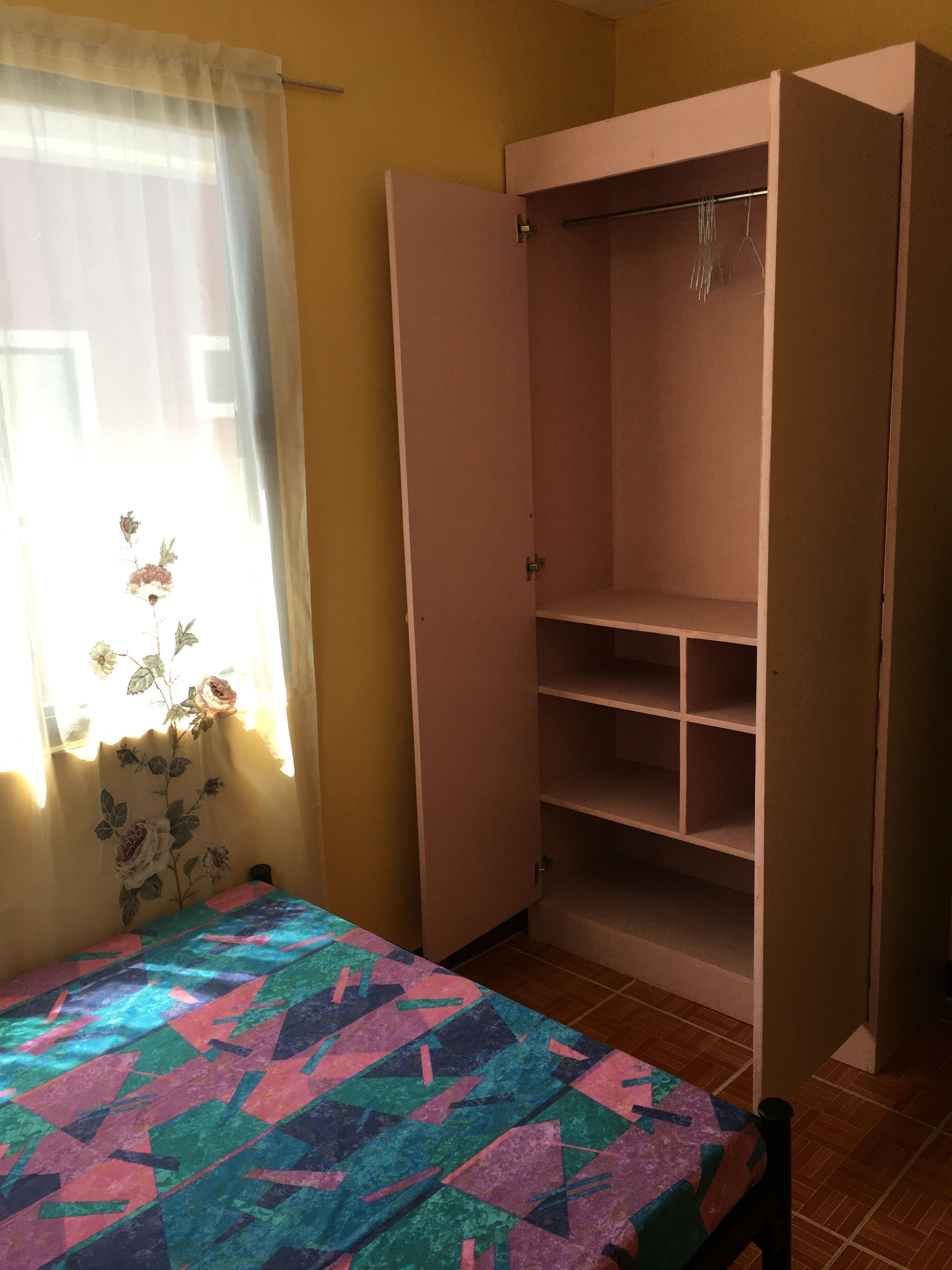 A bedroom with a bed, a wardrobe, and a window with floral curtains.