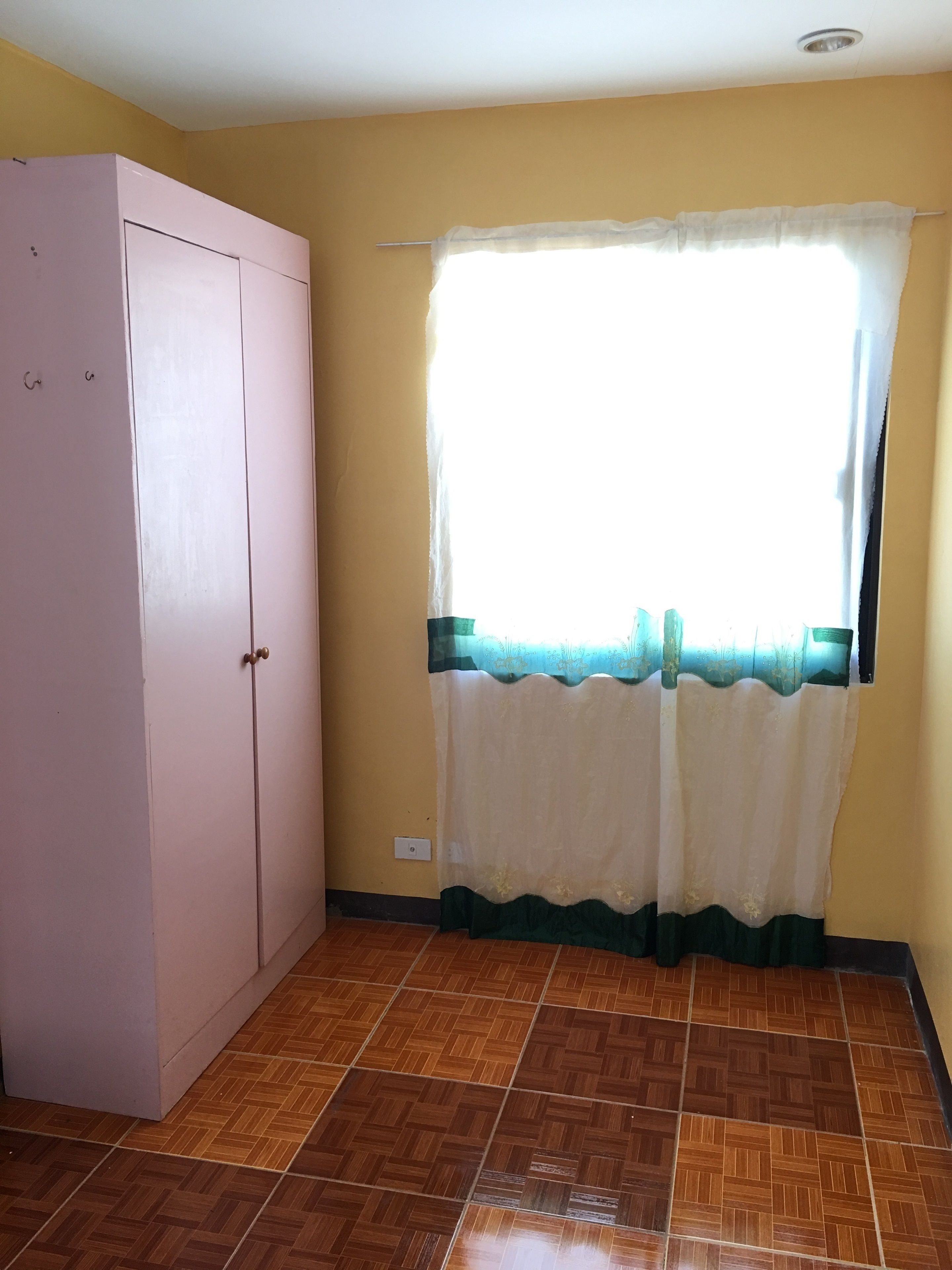 Una habitación con un armario grande, una ventana con cortina translúcida y suelo de baldosas.