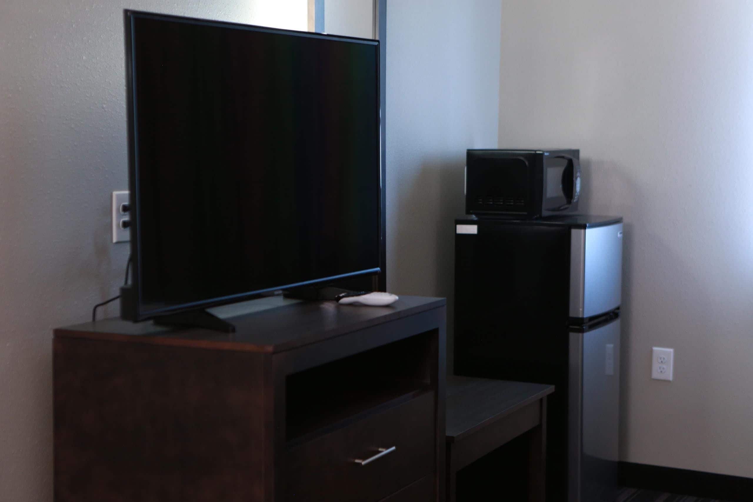 A dark wooden TV stand with a flat-screen TV and a microwave on top.