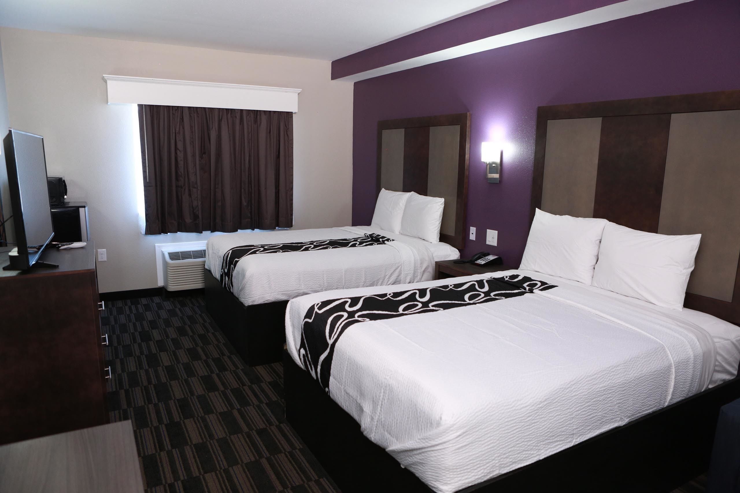 Habitació d'hotel amb dos llits, televisió i finestra amb cortines.