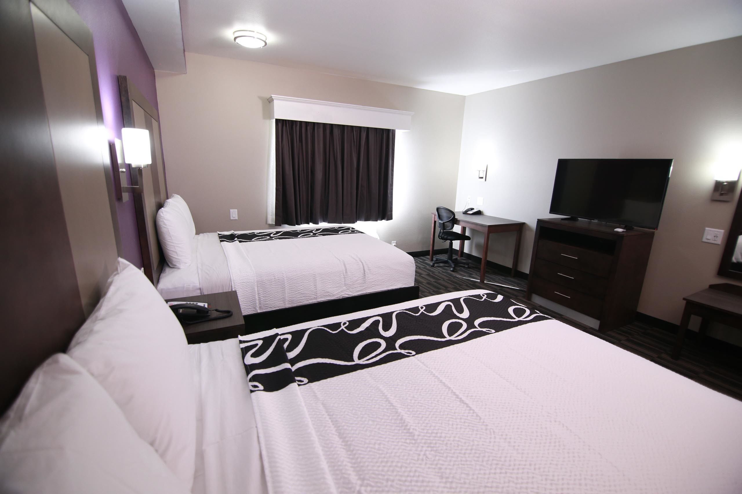 A hotel room with two beds, a desk, a chair, a TV, and a window with curtains.